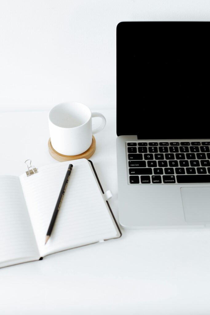 A minimalist workspace featuring a laptop, notebook, and coffee cup in a bright setting.